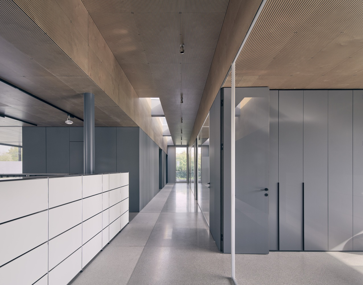 Corridor with white and grey cabinetry beneath angled timber ceiling with skylights