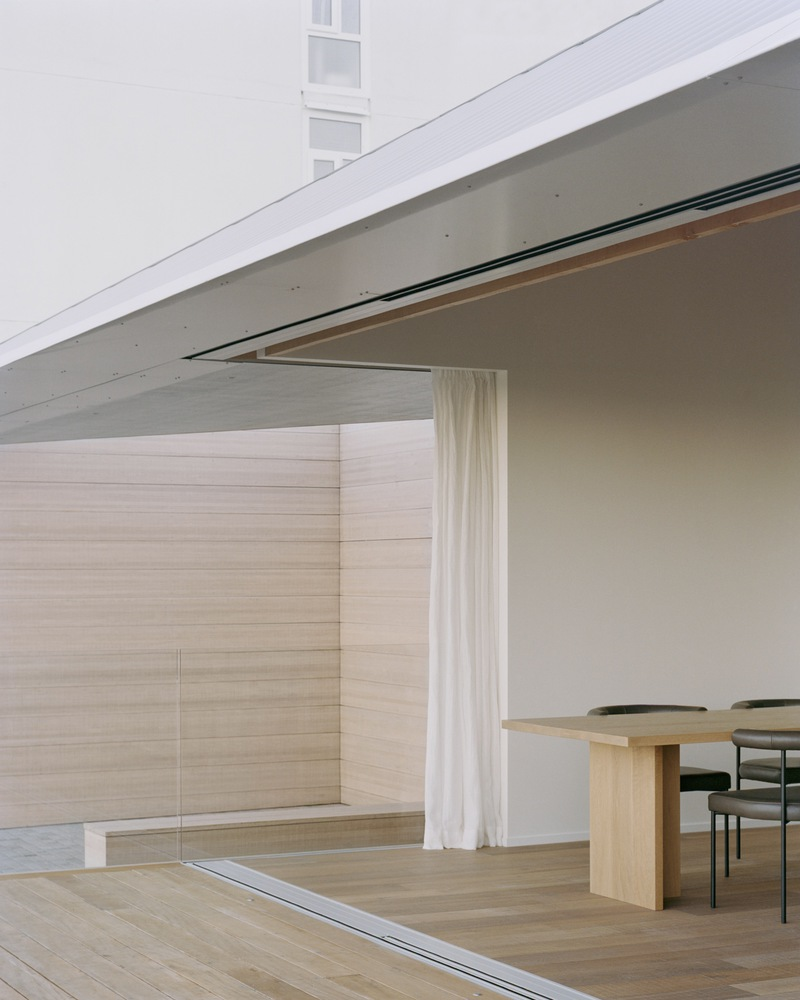 Corner detail of metal standing seam roof meeting timber column and sheer white curtain