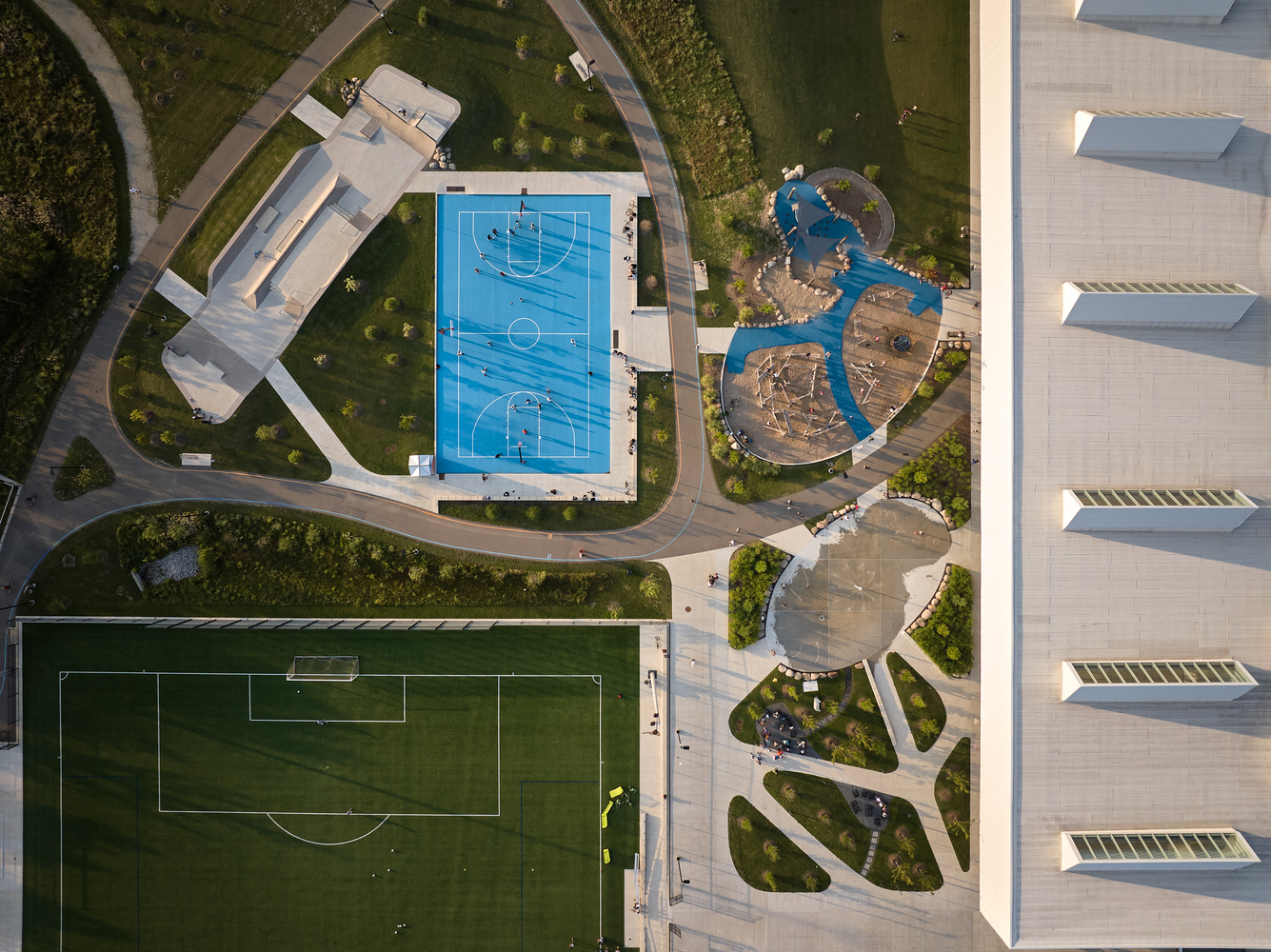 Aerial view of outdoor basketball court and playground beside sawtooth roof building