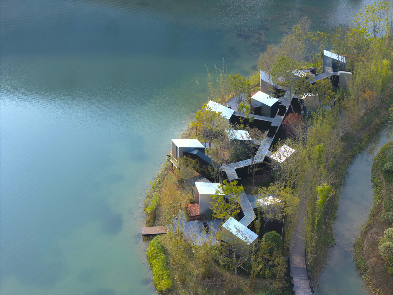Aerial view of white-roofed pavilions clustered along a narrow peninsula surrounded by autumn foliage and water