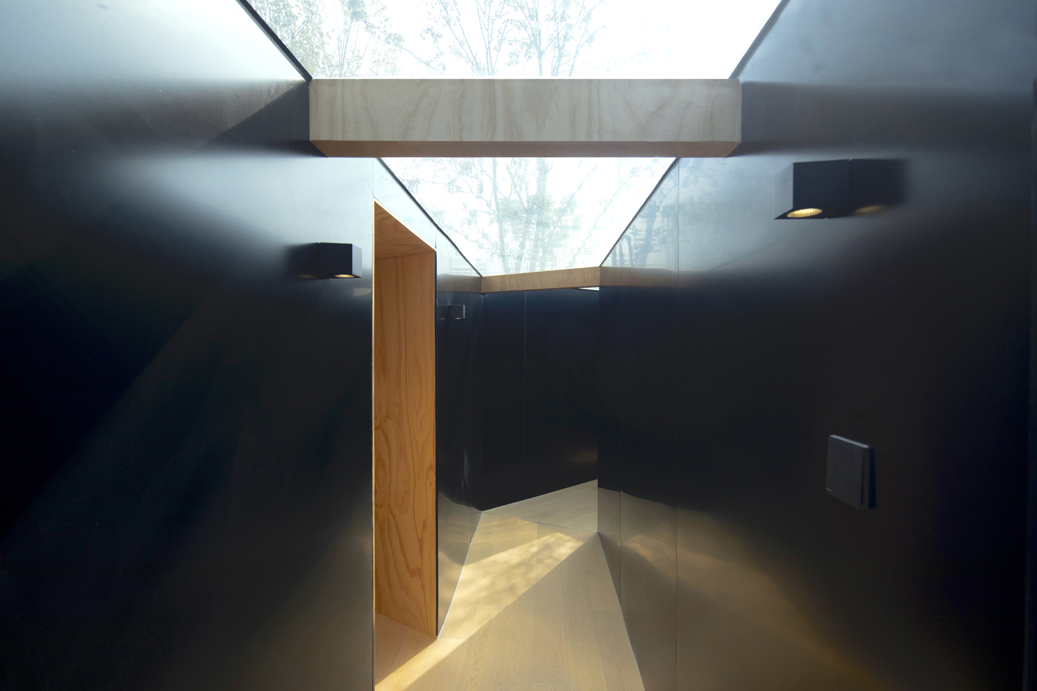 Interior corridor with dark metal walls and timber ceiling beams framing a skylight above