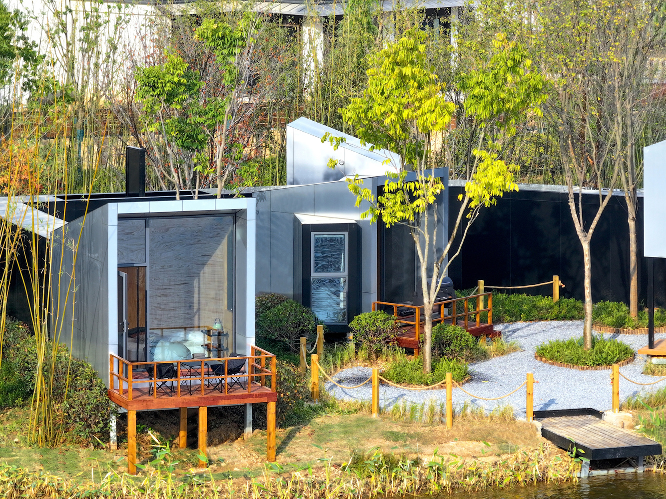 Elevated glass pavilion on timber deck surrounded by bamboo groves and newly planted trees in afternoon sun