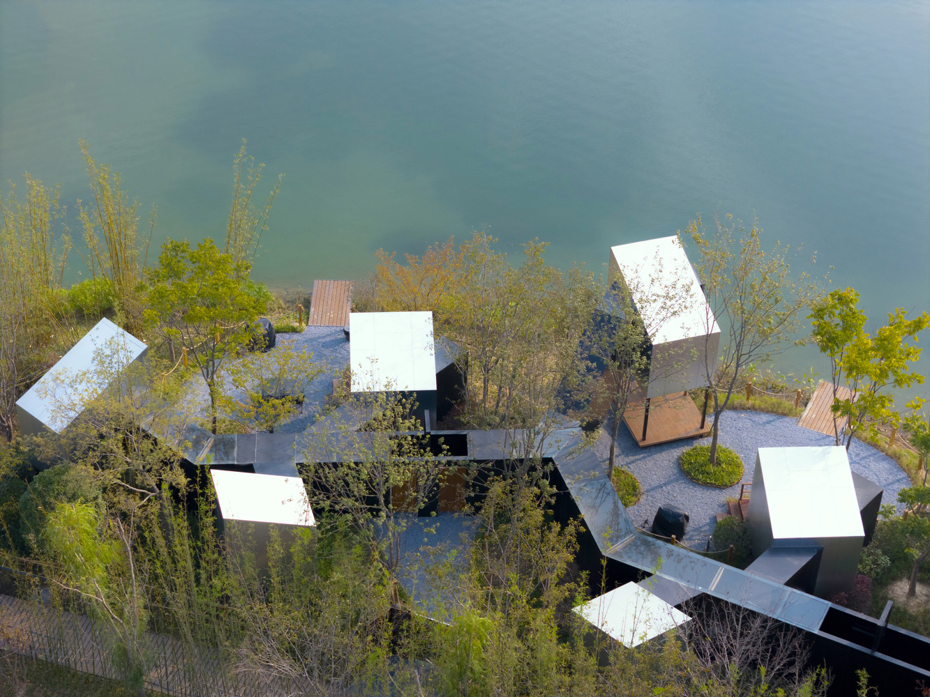 Aerial view of staggered white roof pavilions connected by walkways among spring foliage beside water