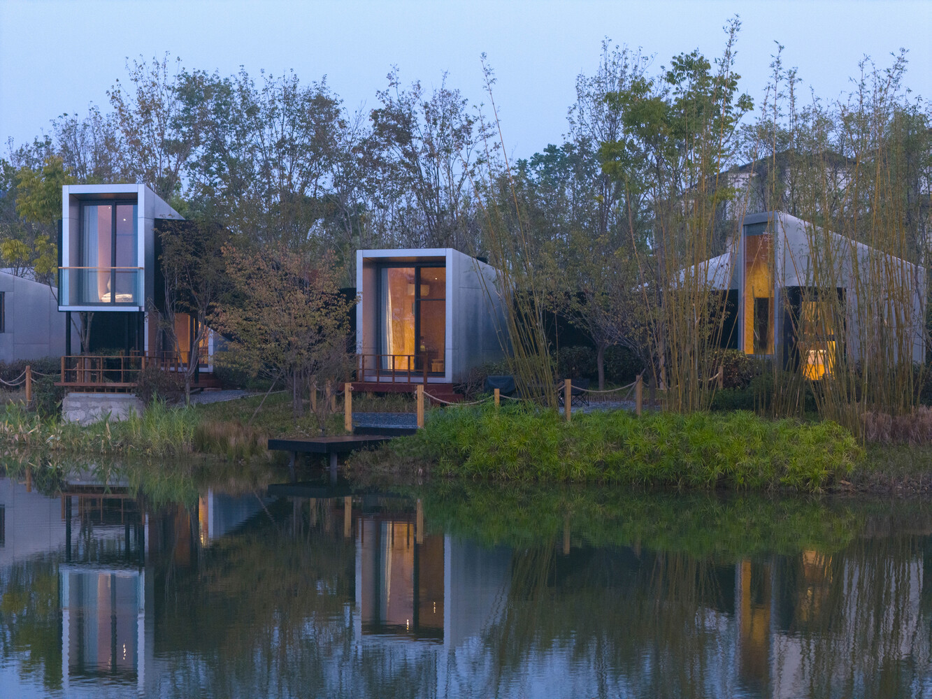 Cluster of curved metal-clad guest pavilions reflected in a still pond at dusk