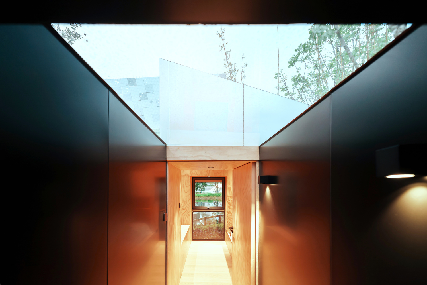 Corridor with rust-colored steel walls and an angled skylight framing trees and sky above