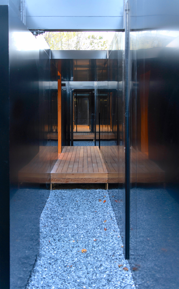 Glass-enclosed entrance with timber deck and gravel courtyard viewed from within a steel-framed corridor