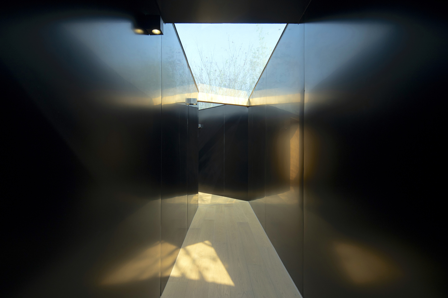 Narrow corridor with angled skylight casting geometric shadows on polished concrete floor