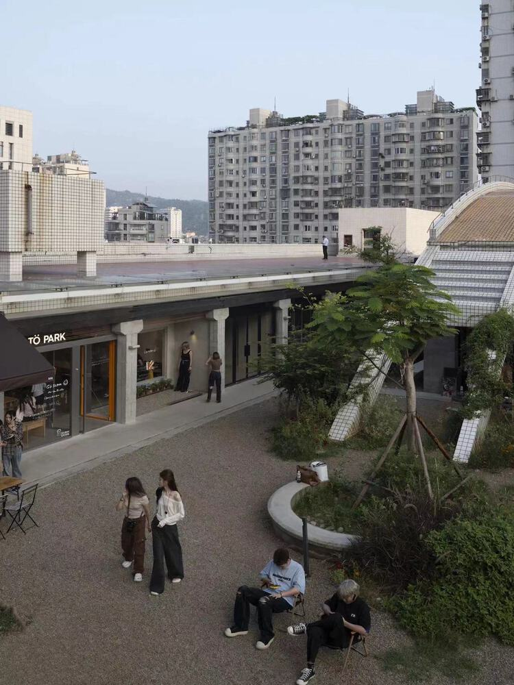 Elevated view of courtyard with curved planting beds and visitors gathered beneath colonnade and tiled canopy