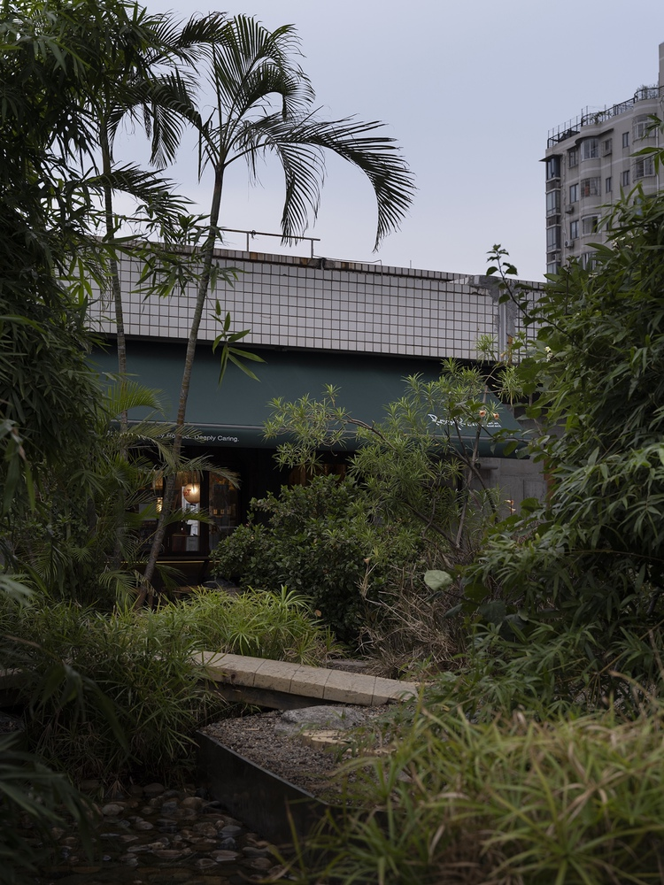 White tiled bridge volume crossing planted courtyard with palm trees at dusk