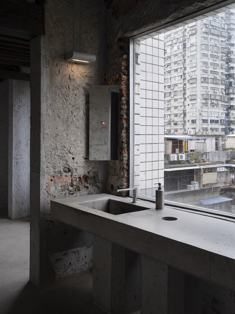 Concrete kitchen counter with sink beside exposed brick wall and gridded window overlooking residential towers