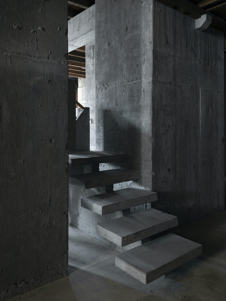 Floating concrete staircase with open risers between exposed concrete walls and columns