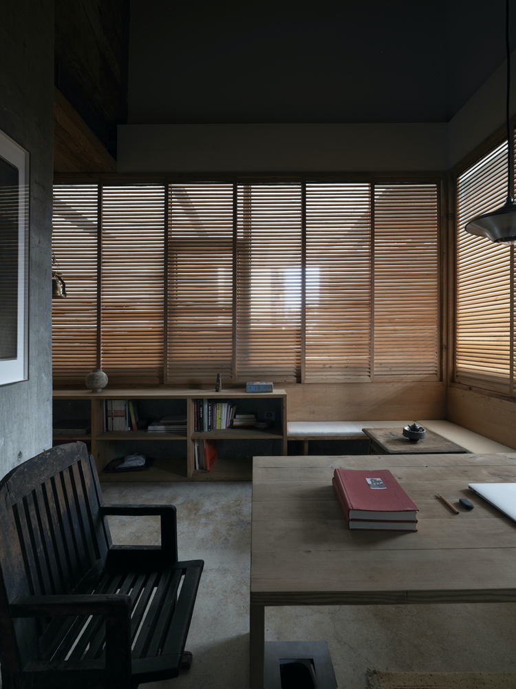 Interior study with wooden slatted windows filtering afternoon light across a low table and bookshelves