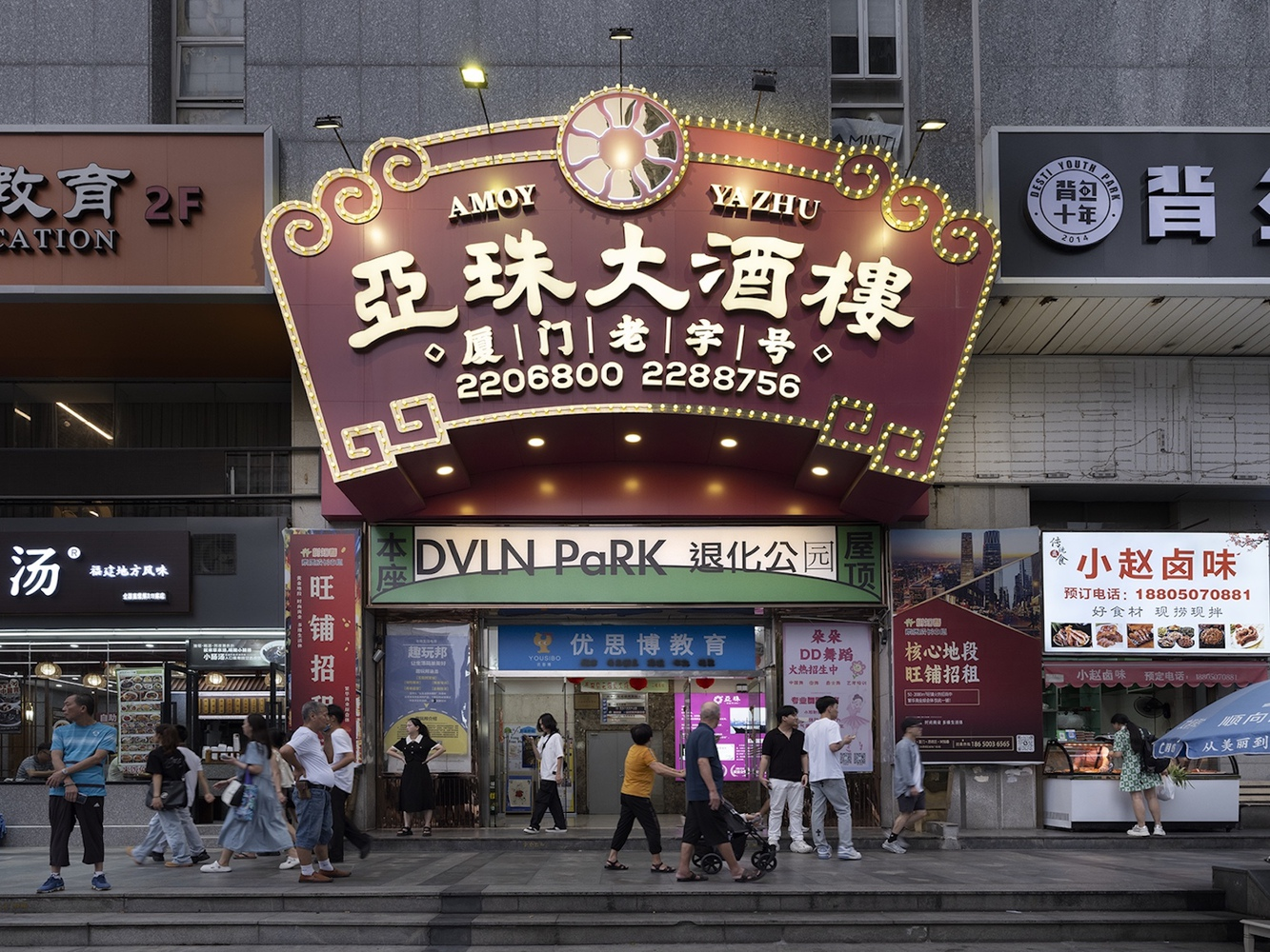 Street-level storefront with illuminated signage and pedestrians passing at dusk
