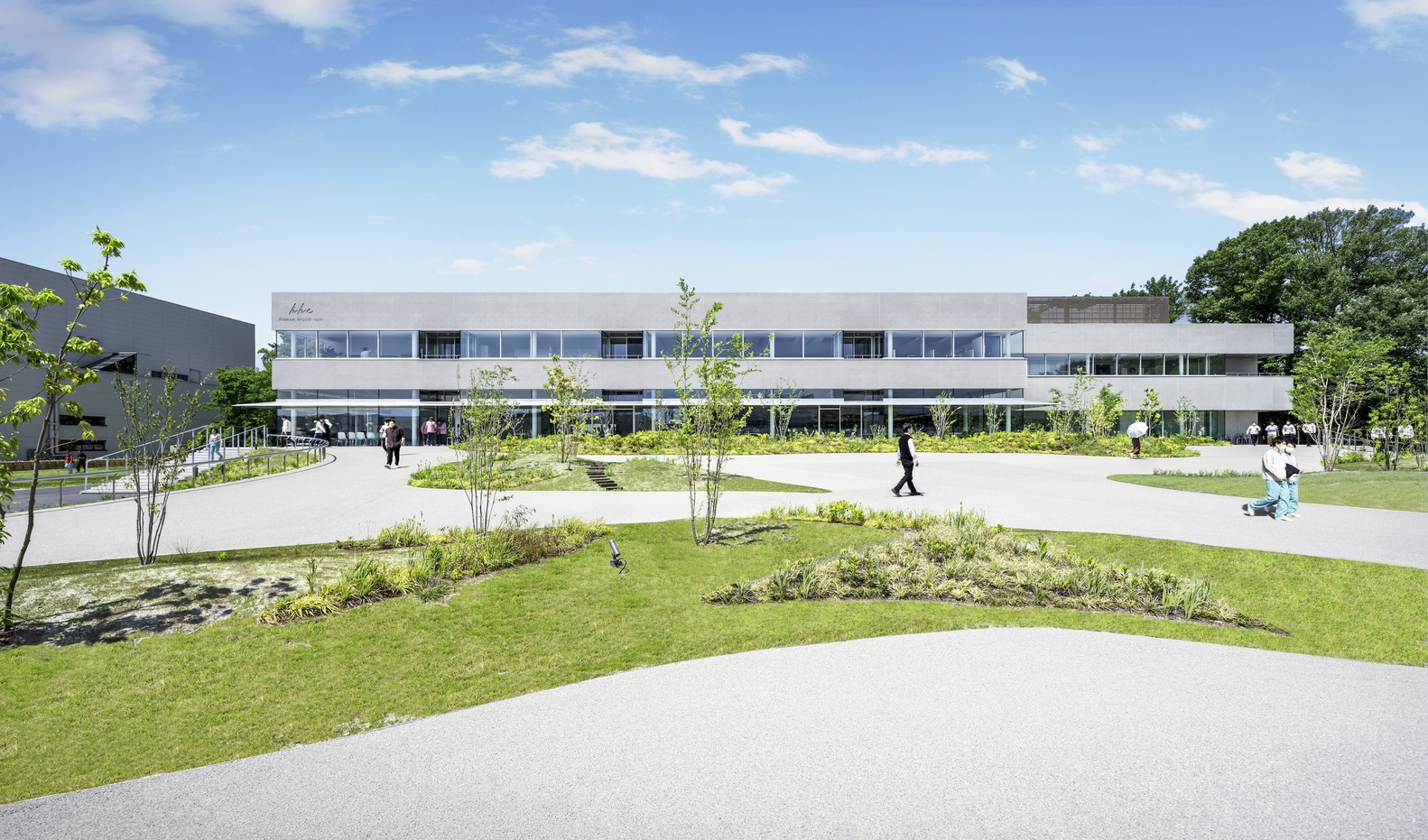 Front facade with horizontal window bands and landscaped courtyard with planted beds and pathways under blue sky