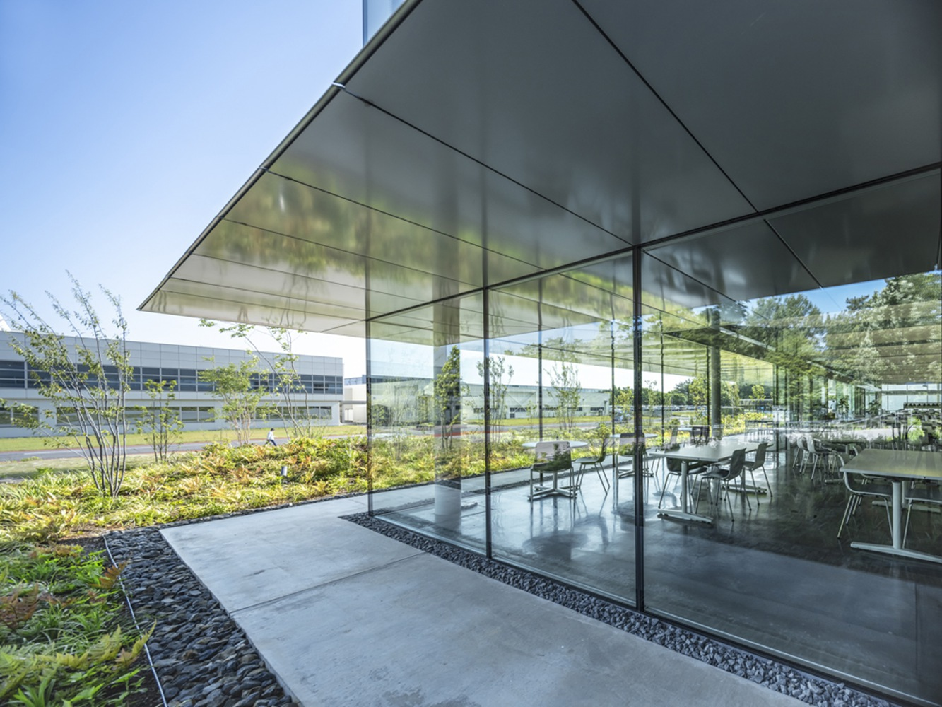 Glass-walled dining area beneath cantilevered canopy with planted beds and pebble borders adjacent to glazed facade