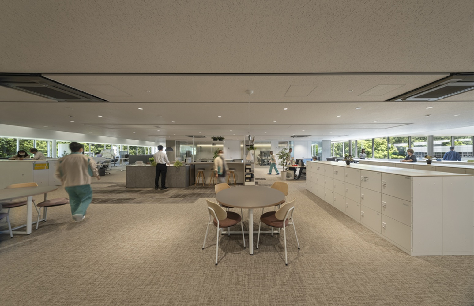 Collaborative workspace with round white table and storage cabinets beneath a suspended ceiling with flush-mounted climate units