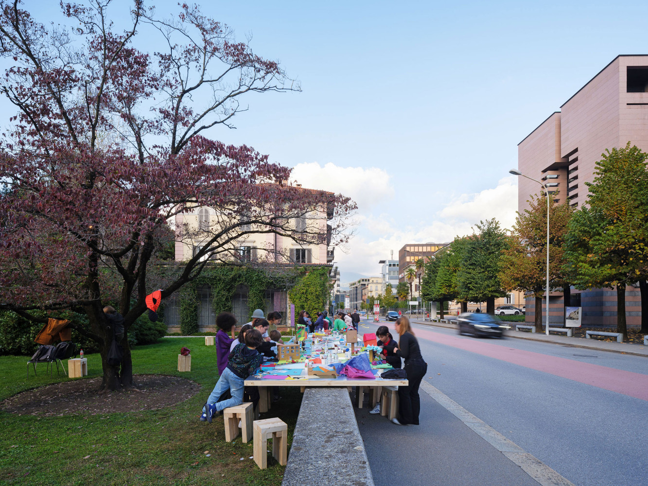 Community table with timber stools on a lawn beside a pedestrian street at dusk