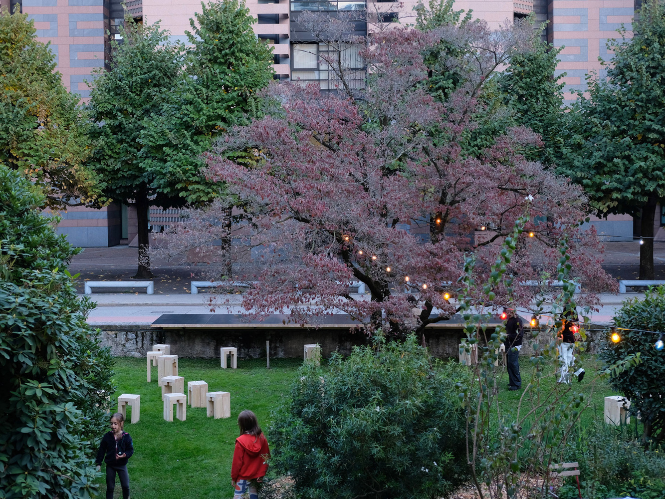 Garden with timber benches and lanterns hung in a bare tree at dusk