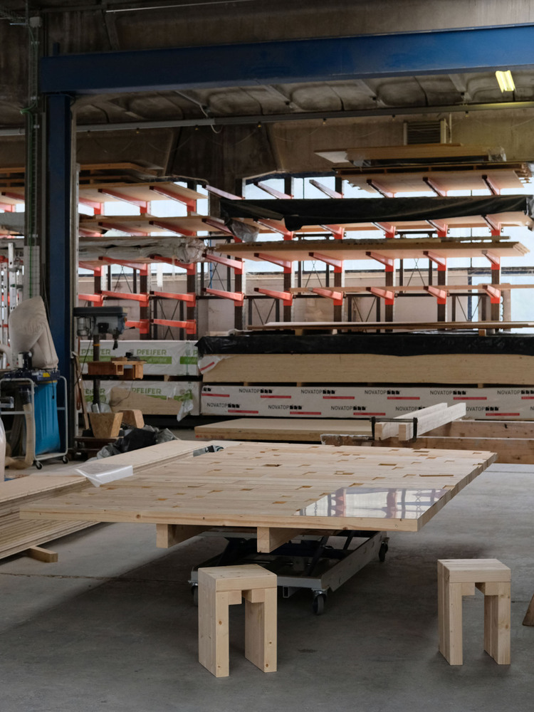 Fabrication shop interior showing cross-laminated timber panels on rolling carts and racked storage systems