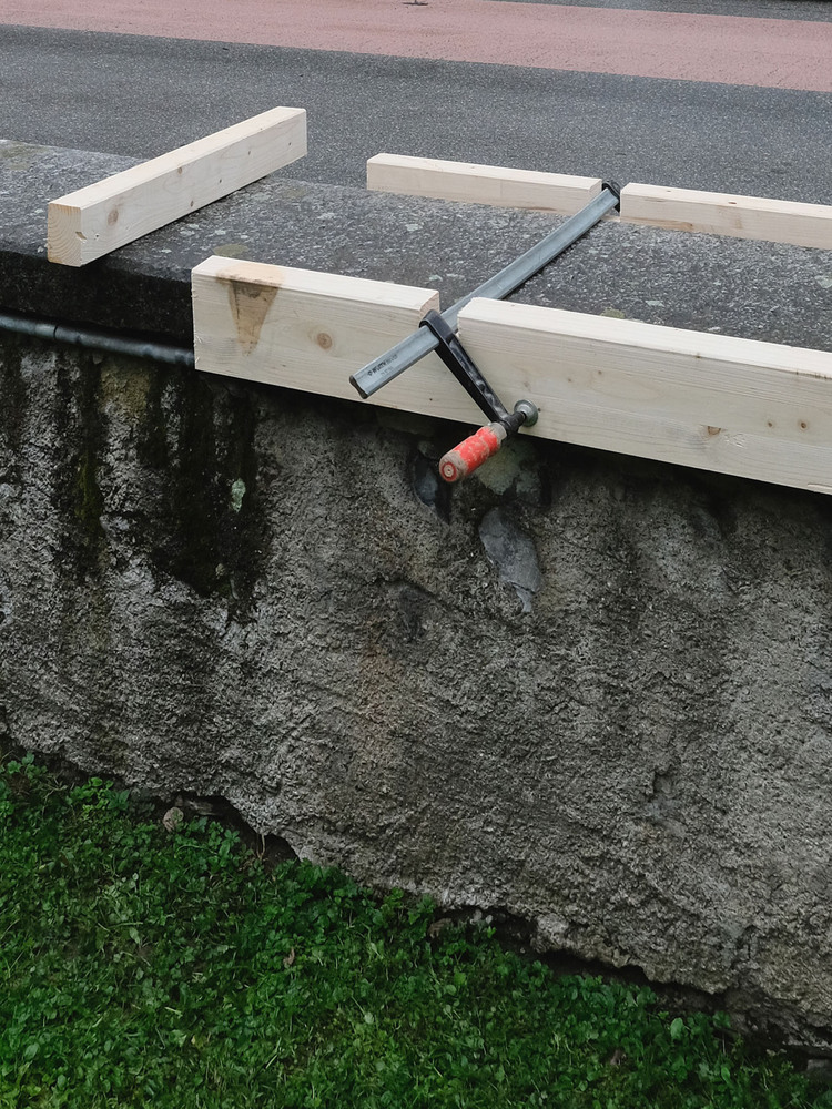 Detail of timber bench frame secured with metal clamps over exposed aggregate concrete base