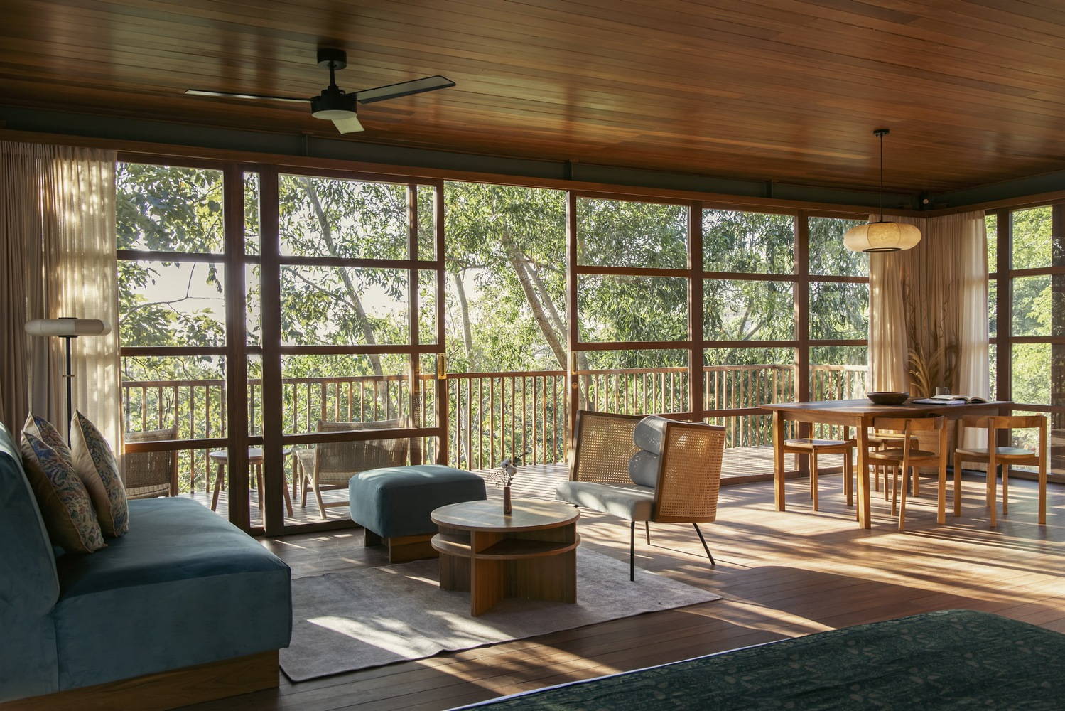 Open living and dining space with timber ceiling and gridded glass doors opening to a balcony amid trees