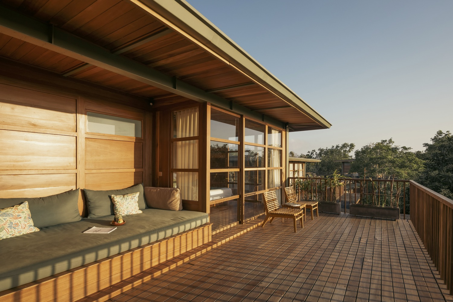 Timber deck with built-in seating and sliding glass doors beneath a deep roof overhang at dusk