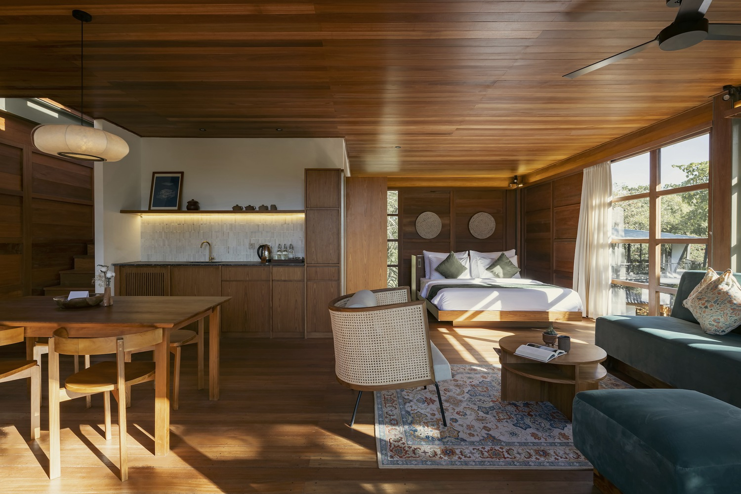 Open-plan suite with kitchenette, dining table, sleeping area and timber ceiling panels in morning sun