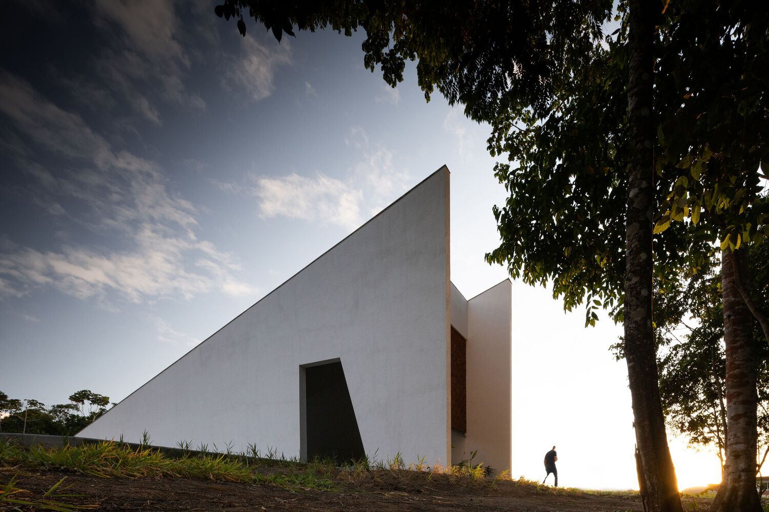 Sloping white wall with recessed opening at golden hour with figure walking in backlit grass