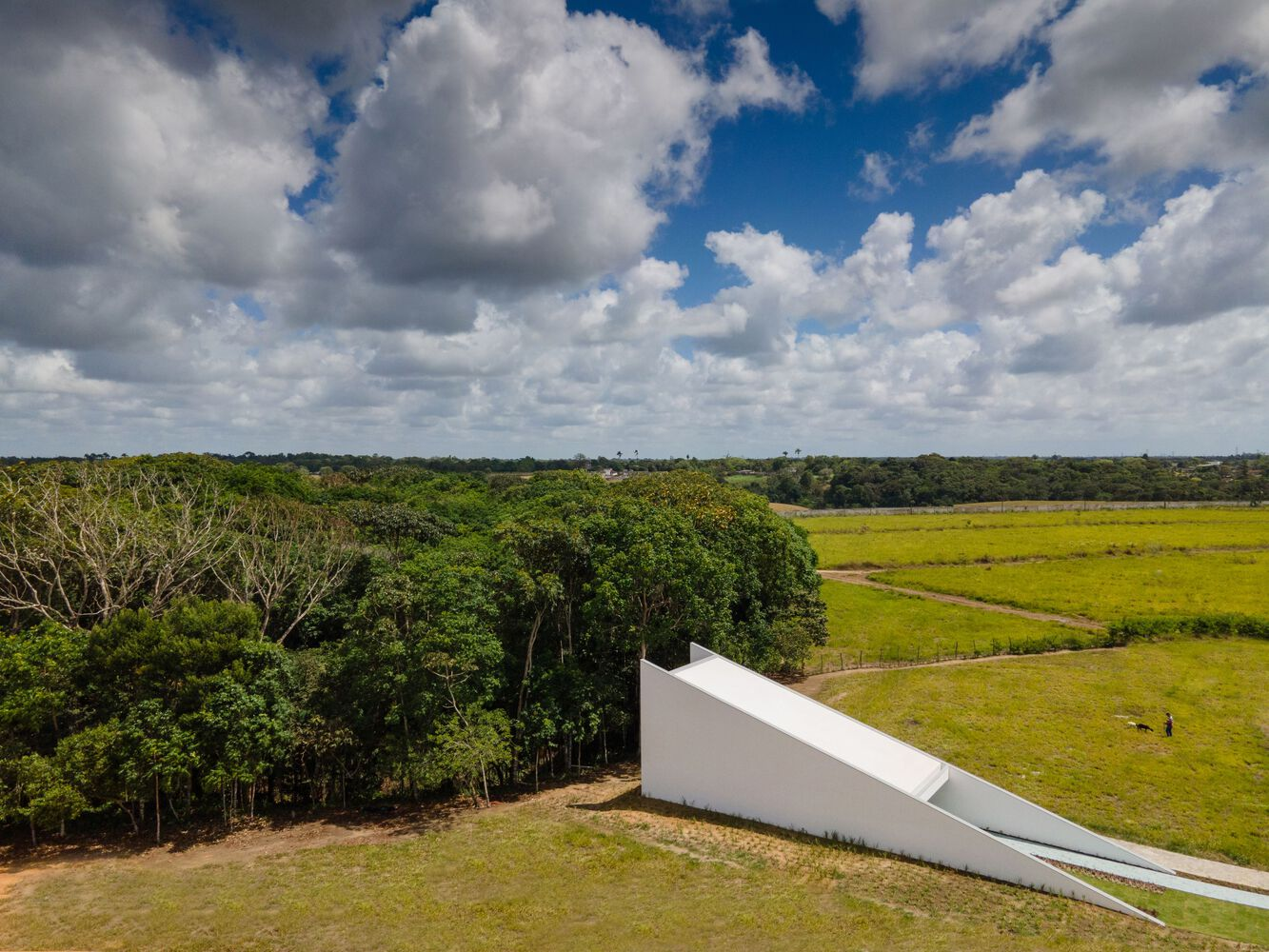 Distant view of the sloped white volume amid tree line and open grassland under cloudy sky