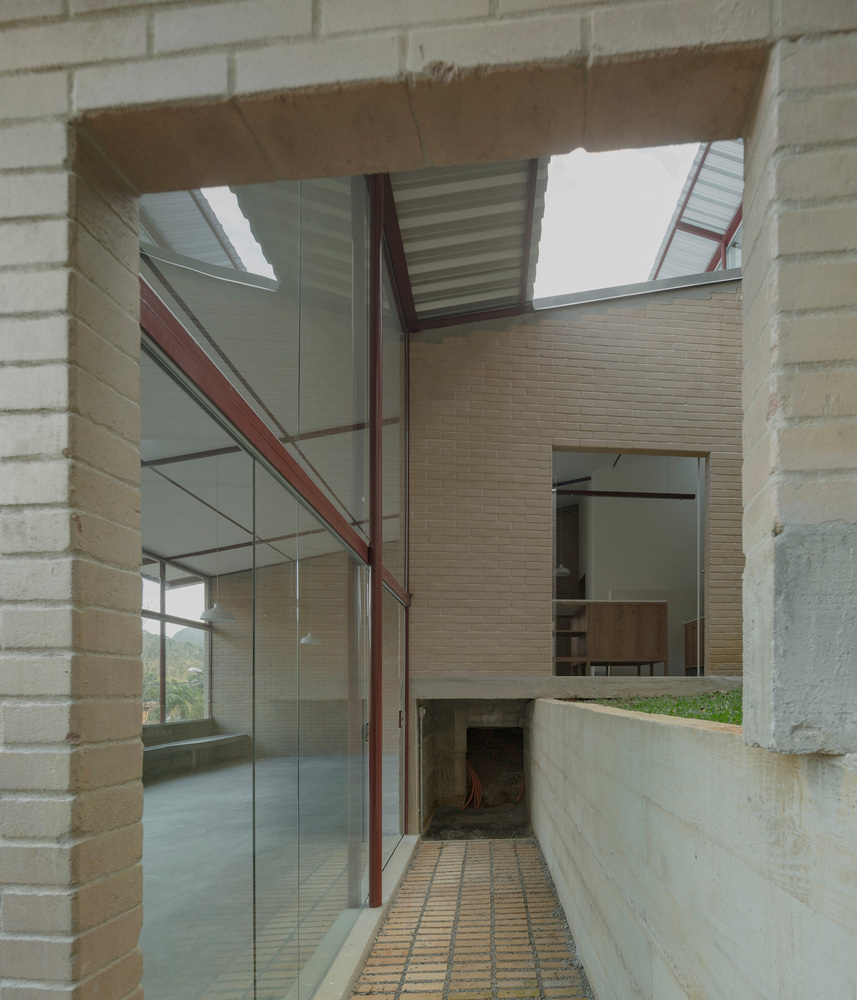 Narrow exterior passageway with buff brick walls, exposed steel frame and gridded tile floor under corrugated metal canopy
