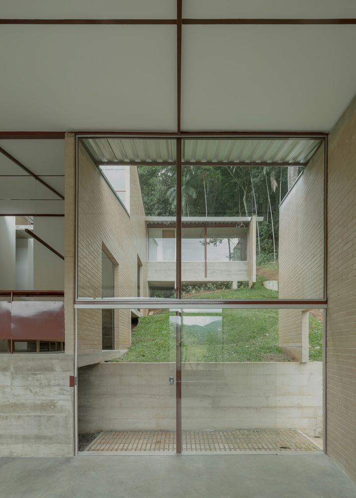 Full-height glazed doorway framing view of courtyard with sloped grass lawn and buff brick walls beyond
