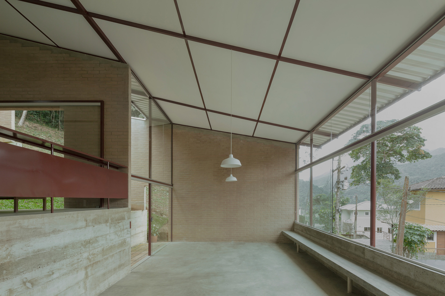 Double-height interior space with exposed steel truss ceiling, pendant lights and floor-to-ceiling windows overlooking hillside