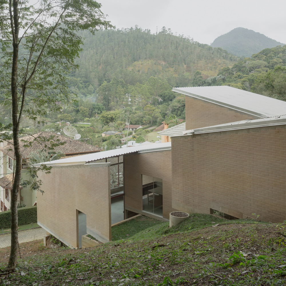 Elevated view of buff brick volumes with corrugated metal roofs nestled into forested hillside under mist