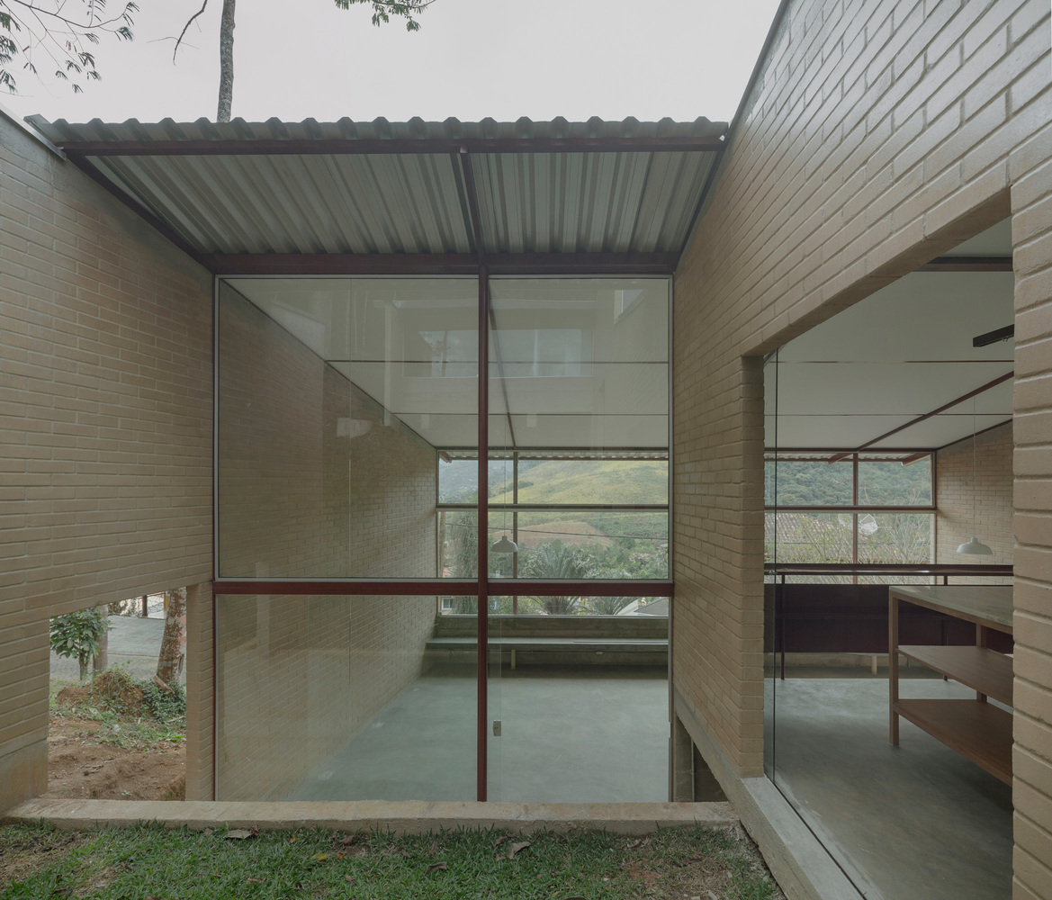 Glass-enclosed courtyard with steel frames and tan brick walls opening to landscape beyond