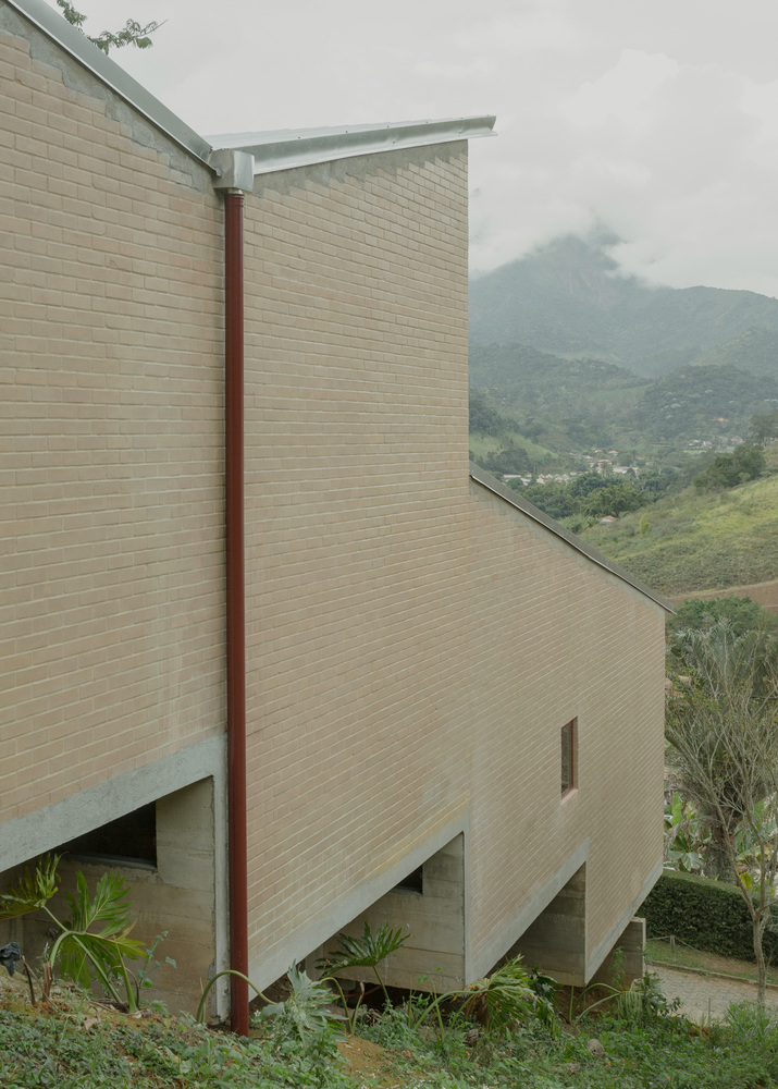 Cantilevered tan brick volumes with metal column framing misty mountain views in the background