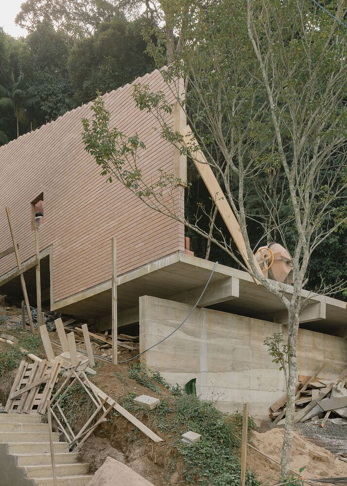 Angled corrugated roof volume on concrete supports surrounded by young trees amid construction debris