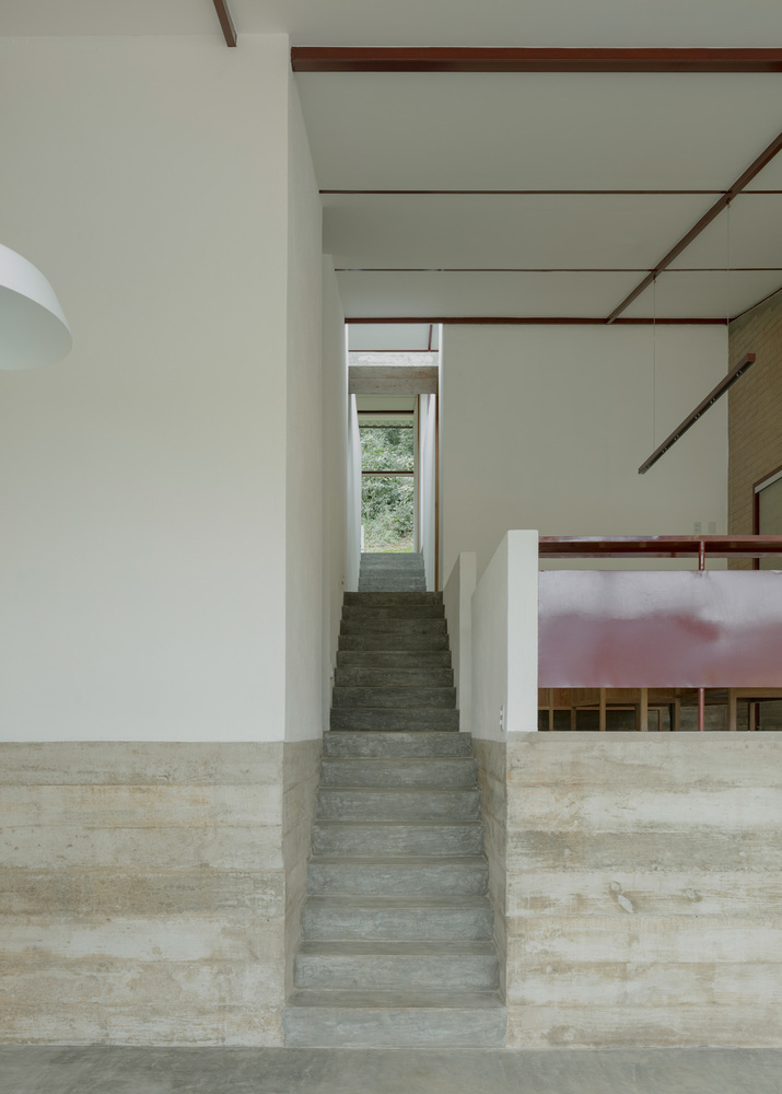 Interior concrete staircase ascending toward window with exposed timber beams crossing white ceiling above