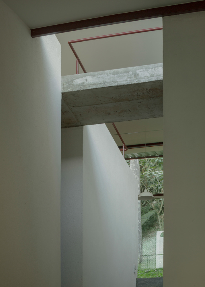 Exposed concrete beam spanning above white walls with a view through to the green garden beyond