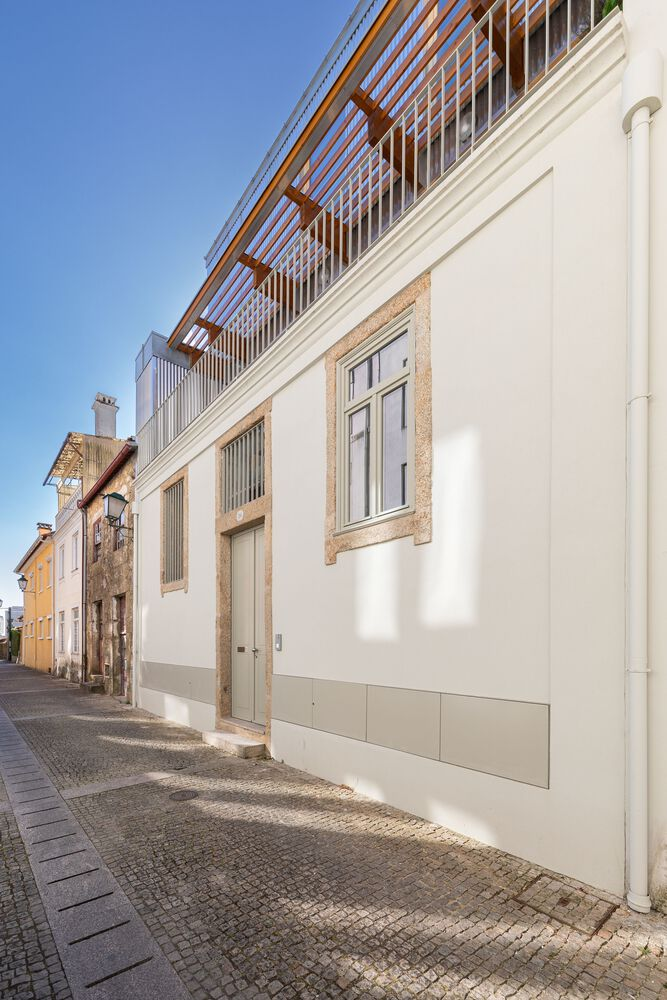 Street view showing white rendered facade with stone-framed door and timber pergola addition above