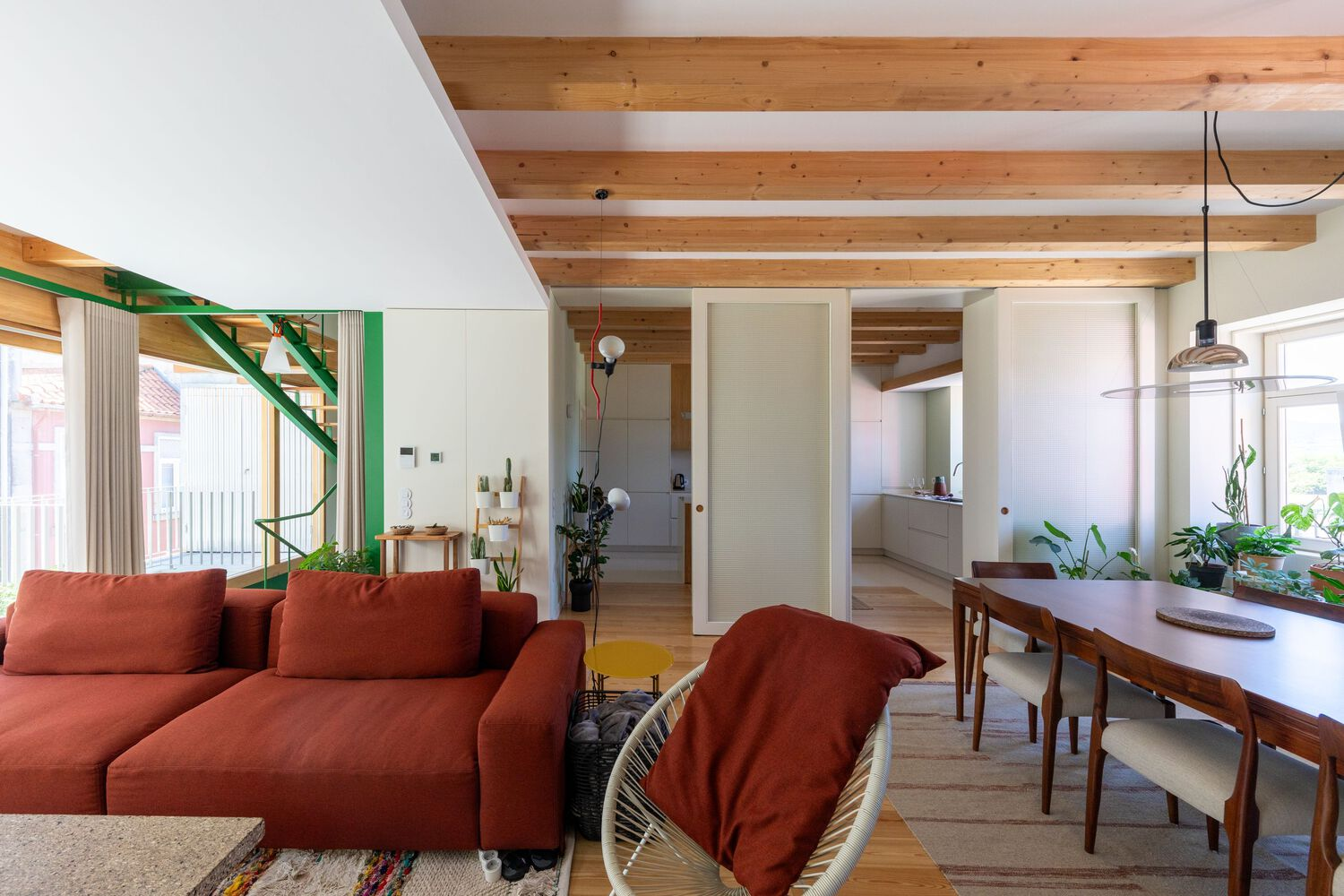Living and dining area with green steel staircase and exposed timber ceiling beams with potted plants