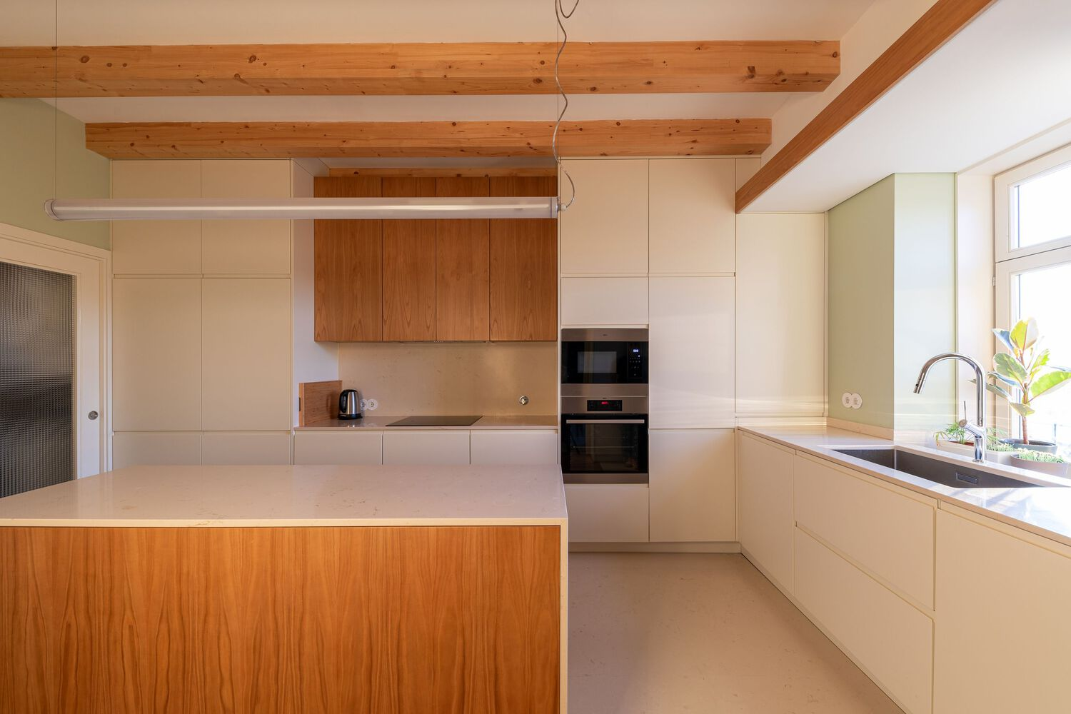 Kitchen with pale wood cabinetry, exposed timber ceiling beams, and a central island with wood panel front