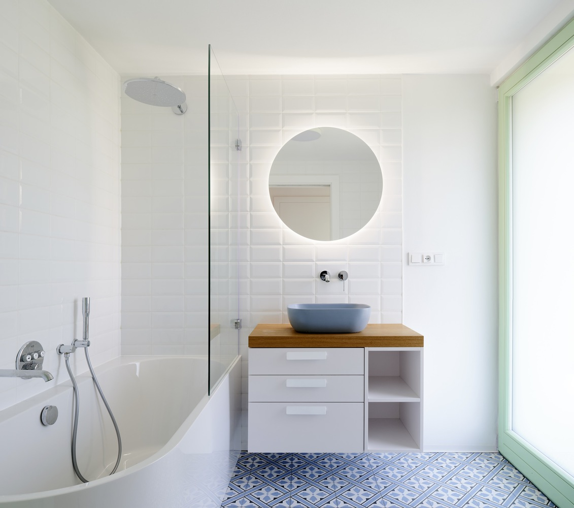 Bathroom with white subway tile wall, backlit round mirror and patterned blue floor tiles