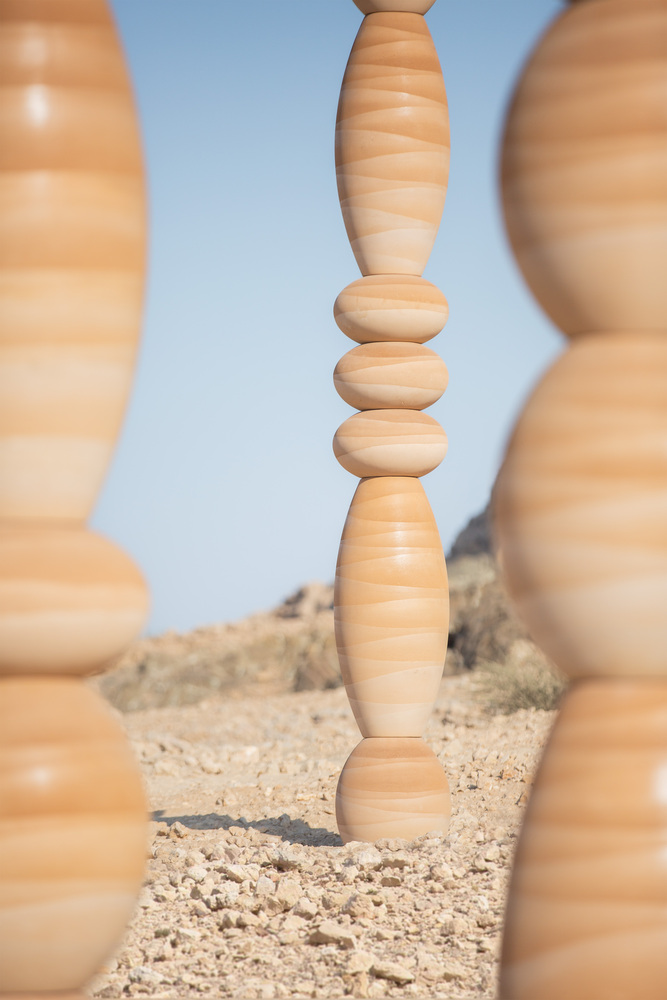 Close view through foreground columns showing the stacked spherical and elliptical segments of a central timber piece
