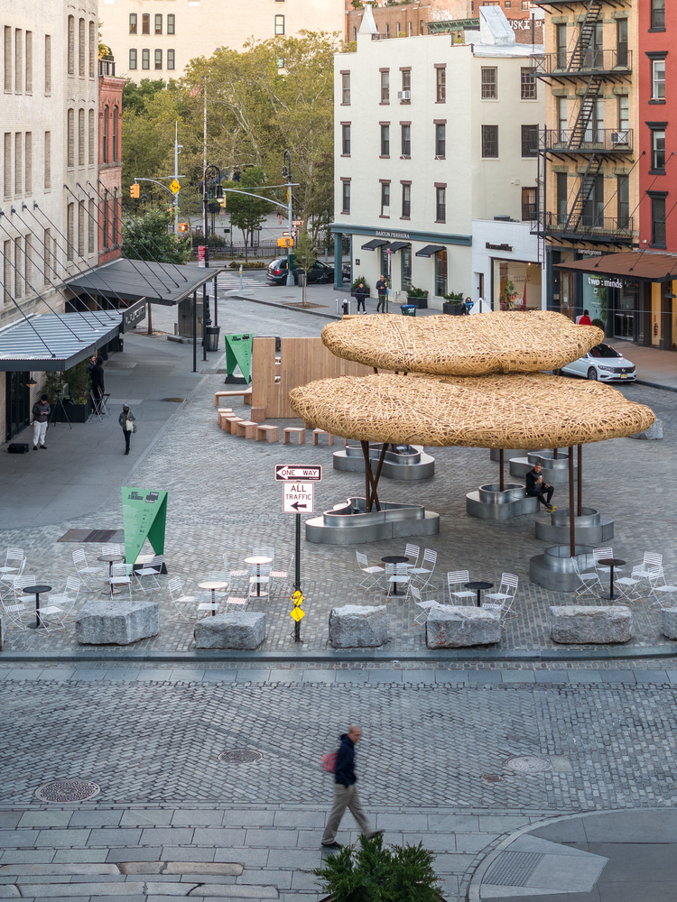Elevated view of woven shade canopies on steel columns in an urban plaza with pedestrians and residential buildings