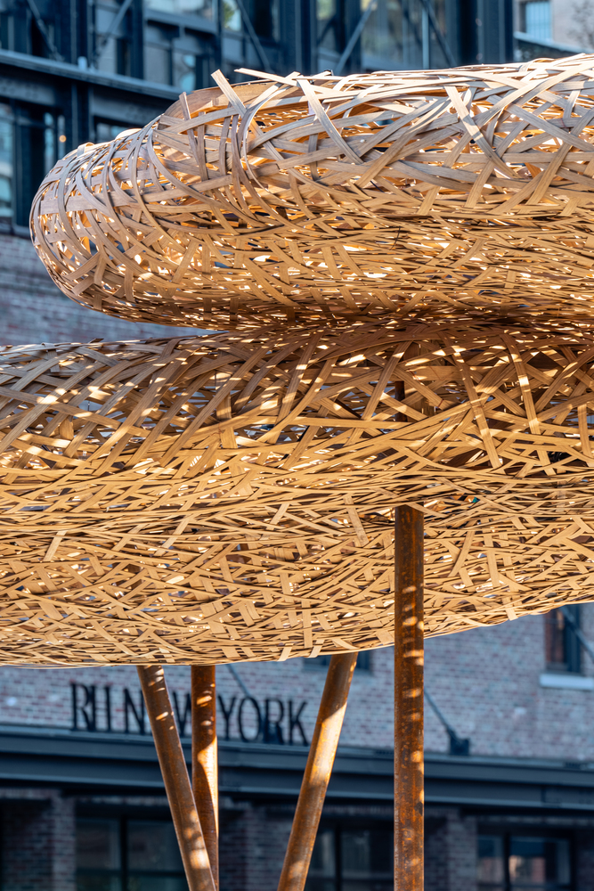 Detail of layered woven timber canopy structure with splayed bronze supports visible beneath