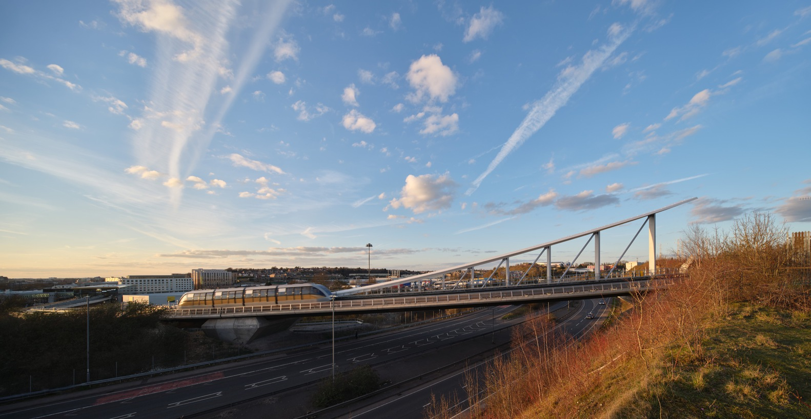 Pedestrian bridge with angled steel truss supports spanning a highway at sunset