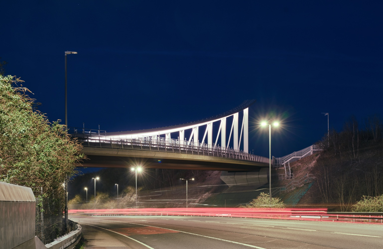 Illuminated pedestrian bridge crossing a motorway at night with light trails below