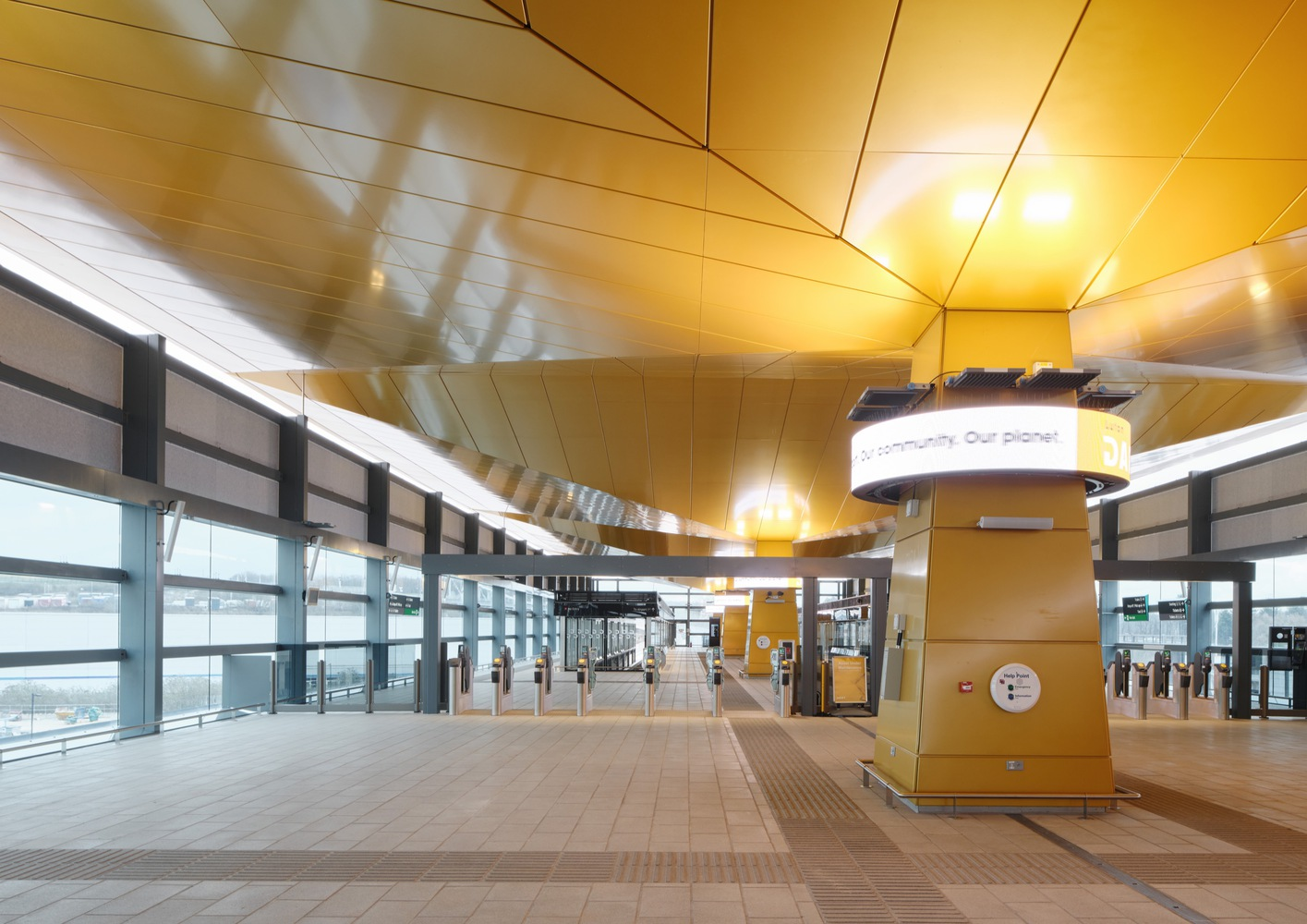 Station platform concourse with geometric gold ceiling panels and glazed curtain wall