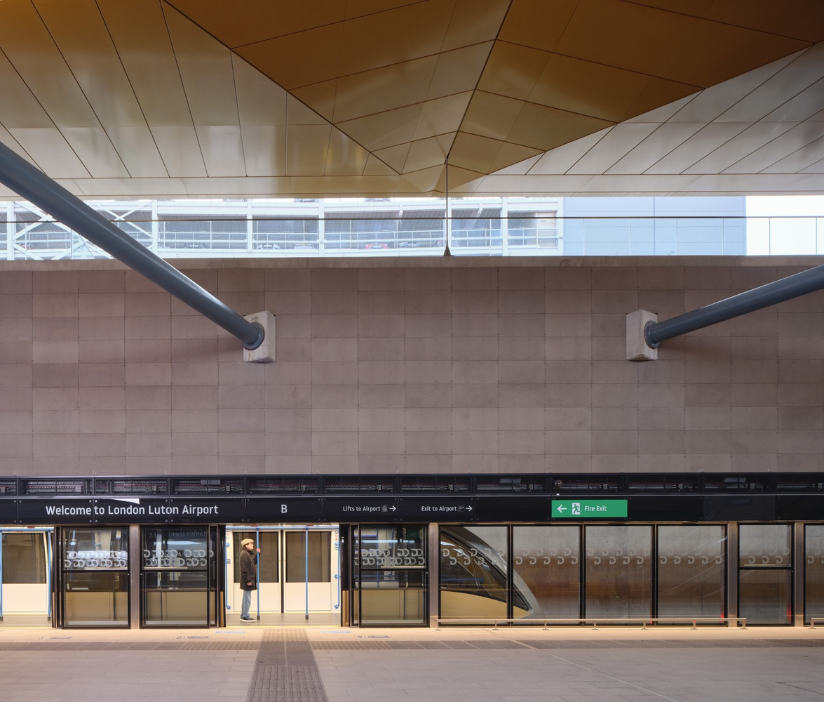 Platform edge showing horizontal tile wall with diagonal grey support beams and white clerestory