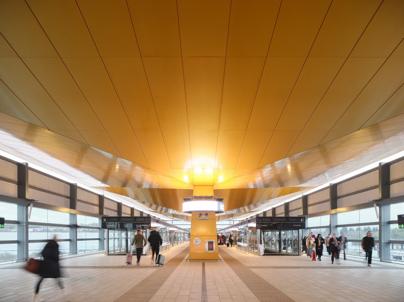 Transit platform with timber-clad ceiling radiating from a central column and commuters passing through